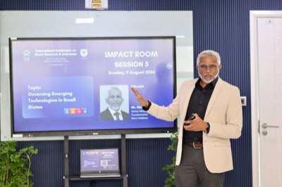 Mohamed Shareef in a light jacket, gesturing towards a screen announcing his session, Governing Emerging Technologies in Small States